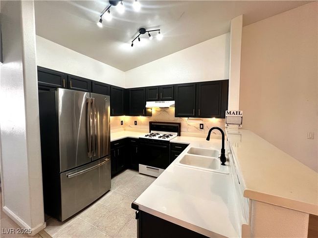 Kitchen with white range with gas stovetop, dark cabinetry, under cabinet range hood, and freestanding refrigerator | Image 7