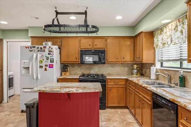Kitchen featuring black appliances, brown cabinetry, a kitchen island, a textured ceiling, and recessed lighting | Image 13