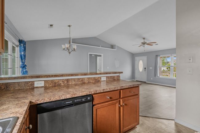 Kitchen featuring stainless steel dishwasher, lofted ceiling, a chandelier, brown cabinetry, and open floor plan | Image 22