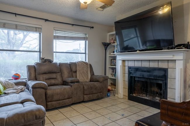 Living area with a textured ceiling, light tile patterned floors, a tile fireplace, and a ceiling fan | Image 18