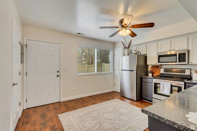 Kitchen with dark wood-style flooring, visible vents, stainless steel appliances, dark countertops, and a ceiling fan | Image 4
