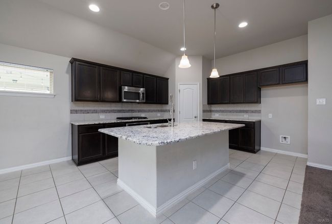 Kitchen featuring appliances with stainless steel finishes, decorative backsplash, light tile patterned floors, an island with sink, and light stone countertops | Image 18