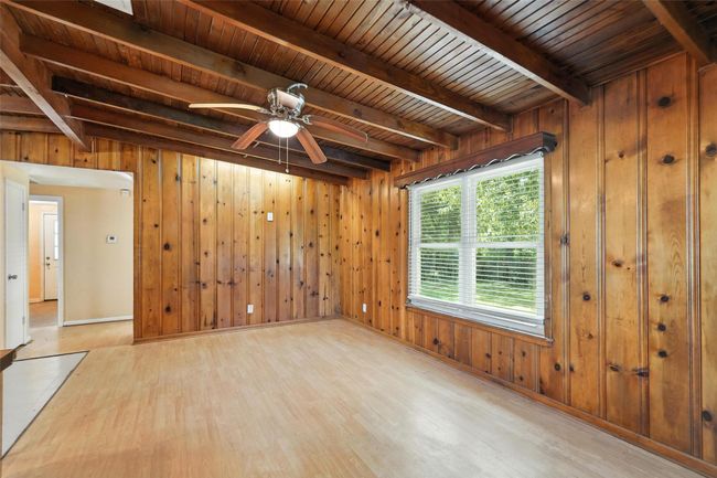 Empty room with wood finished floors, wooden walls, a wooden ceiling with exposed beams, and a ceiling fan | Image 14