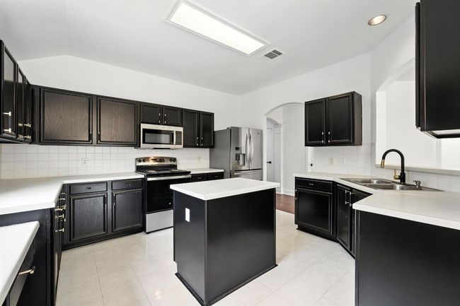 The remodeled kitchen is a true centerpiece, showcasing freshly painted cabinetry with designer hardware, abundant counter and cabinet space, a center island, built-in workstation, and brand-new stainless steel oven/range and microwave. | Image 6
