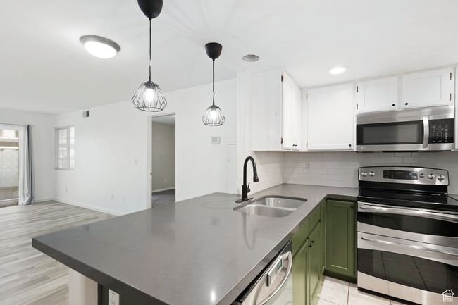 Kitchen with tasteful backsplash, appliances with stainless steel finishes, a peninsula, white cabinets, and a sink | Image 9