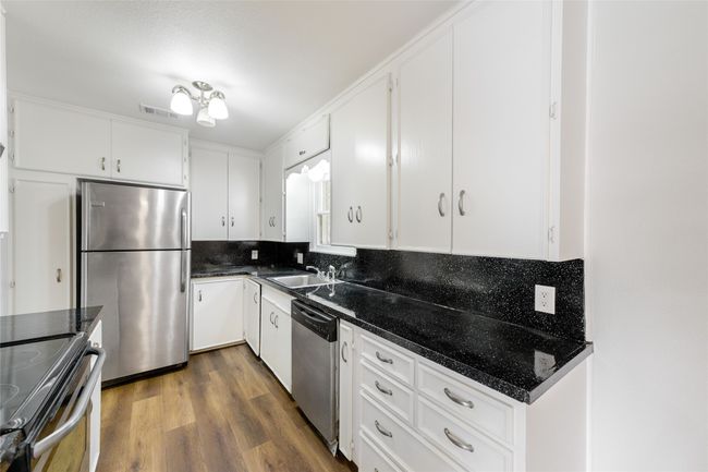 Kitchen with appliances with stainless steel finishes, tasteful backsplash, white cabinets, dark wood-style floors, and dark stone countertops | Image 13