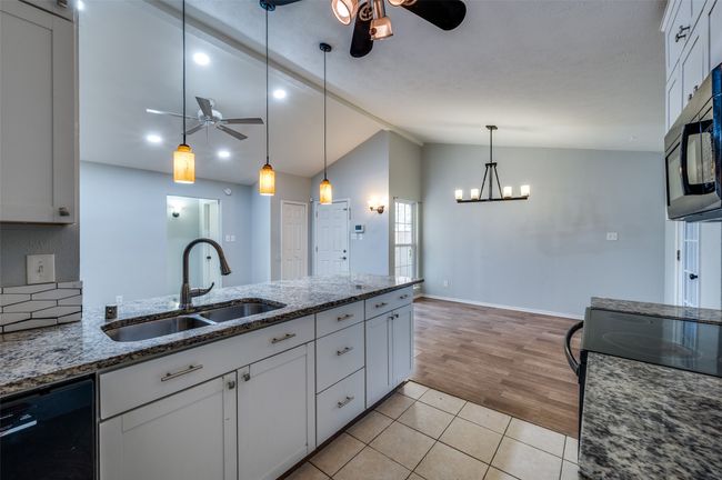 Kitchen with ceiling fan, black appliances, vaulted ceiling, dark stone countertops, and white cabinets | Image 9