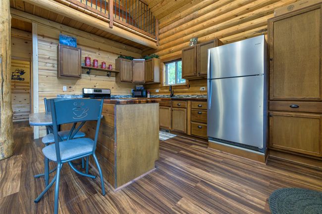Kitchen with a kitchen island, open shelves, appliances with stainless steel finishes, dark wood-style floors, and log walls | Image 7