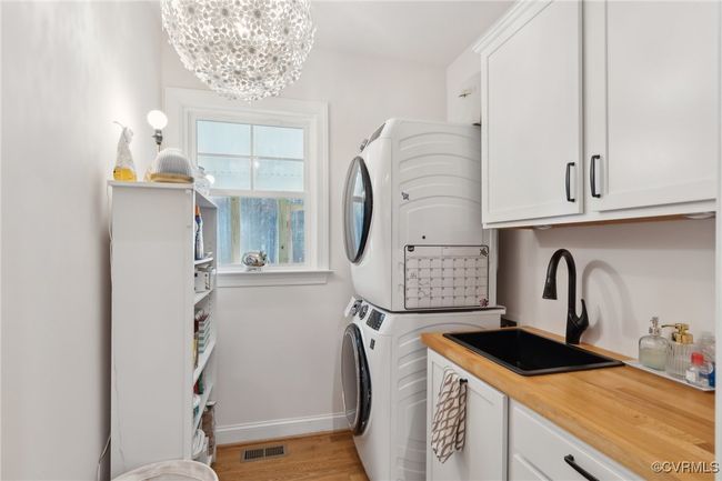 Clothes washing area featuring visible vents, stacked washing maching and dryer, cabinet space, a sink, and a chandelier | Image 34