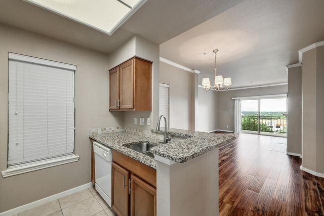 Kitchen featuring white dishwasher, brown cabinets, light stone countertops, open floor plan, and a chandelier | Image 15