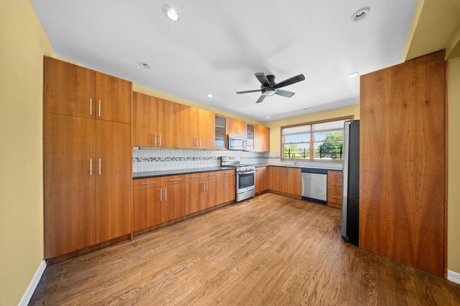 Kitchen with appliances with stainless steel finishes, brown cabinetry, wood finished floors, tasteful backsplash, and a ceiling fan | Image 14