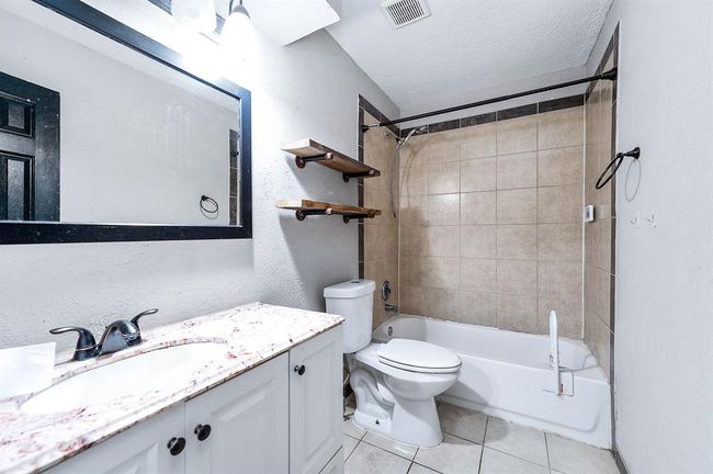 This bathroom features a modern design with a granite countertop, under-mount sink, and dark fixtures. It includes a bathtub with tiled walls, open wooden shelves, and a large mirror, combining functionality with style. | Image 15