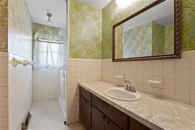Full bath featuring wallpapered walls, wainscoting, vanity, and tile walls | Image 15