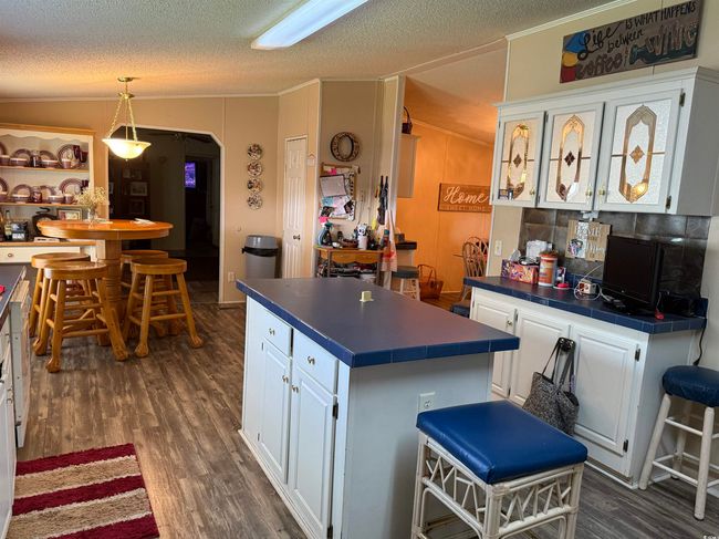 Kitchen featuring white cabinets, ornamental molding, dark wood finished floors, a textured ceiling, and tile counters | Image 8