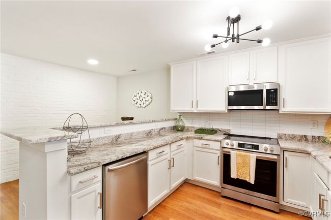 Kitchen with appliances with stainless steel finishes, a peninsula, light wood-type flooring, white cabinets, and backsplash | Image 7