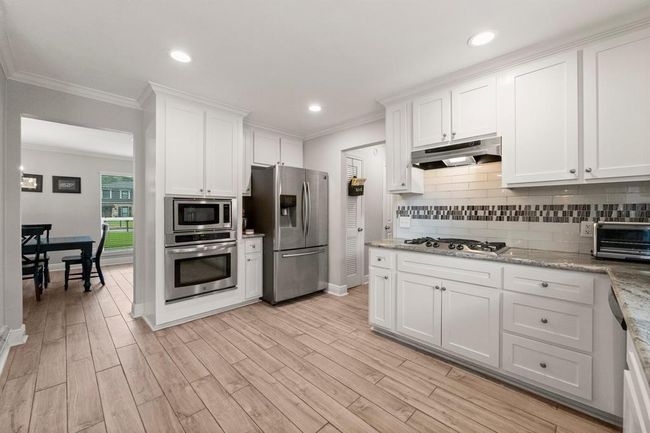The kitchen features modern stainless steel appliances, white cabinetry, and a stylish backsplash. The open layout connects seamlessly to a dining area. | Image 12
