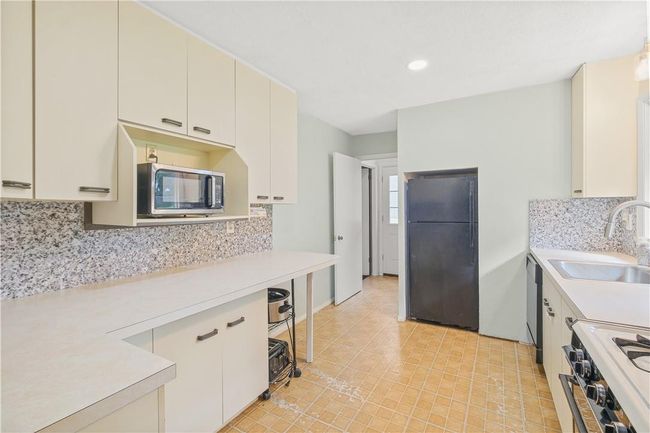 Kitchen featuring black refrigerator, sink, backsplash, and white stove | Image 6