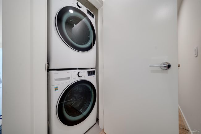 Laundry area featuring stacked washing machine and dryer, light wood-type flooring, and baseboards | Image 12