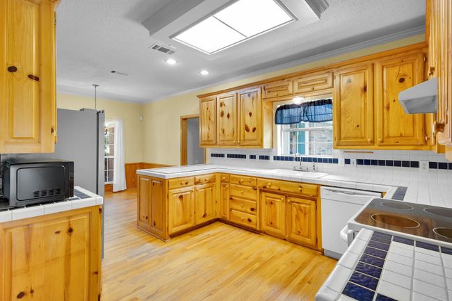 Kitchen with a peninsula, dishwasher, under cabinet range hood, light wood finished floors, and tile countertops | Image 7