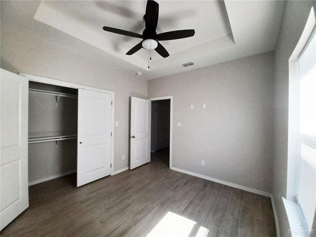 Unfurnished bedroom with a raised ceiling, wood finished floors, baseboards, a closet, and ceiling fan | Image 6