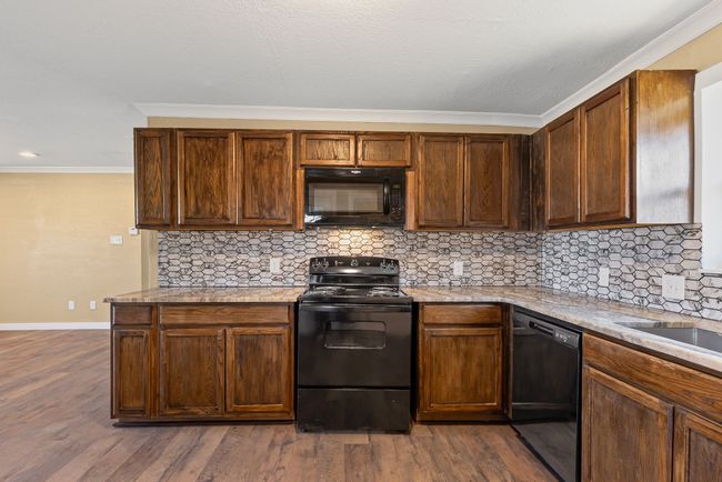 Kitchen featuring dark wood-type flooring, crown molding, black appliances, and tasteful backsplash | Image 13