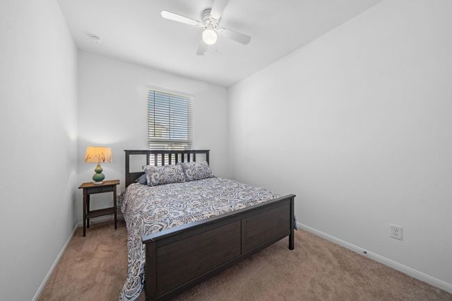 This bedroom with an ensuite bath features white walls and a white ceiling fan, creating a clean and bright atmosphere. | Image 6