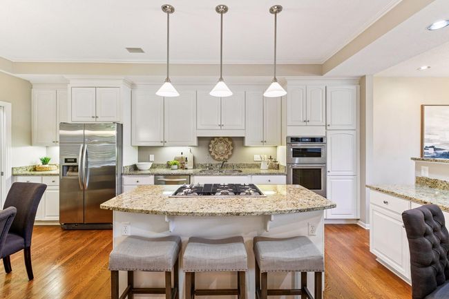 Gourmet kitchen with white Shaker cabinets, granite countertops, and a spacious center island with bar seating. | Image 11