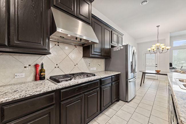 Kitchen featuring under cabinet range hood, stainless steel appliances, a chandelier, light tile patterned floors, and tasteful backsplash | Image 10