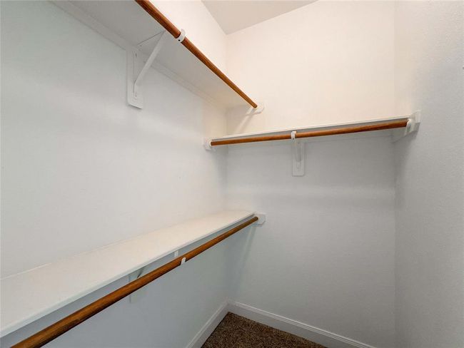 This photo shows a spacious walk-in closet with multiple wooden hanging rods and white shelving, perfect for organized storage. | Image 19