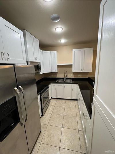 Kitchen with light tile patterned floors, sink, stainless steel range, white cabinets, and refrigerator | Image 2