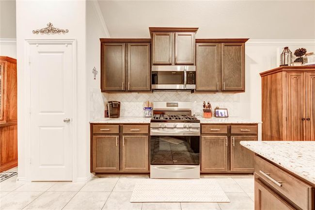 Open concept kitchen with dark wood cabinets, farmhouse sink, gas stovetop and oven, granite countertops, and pantry | Image 10