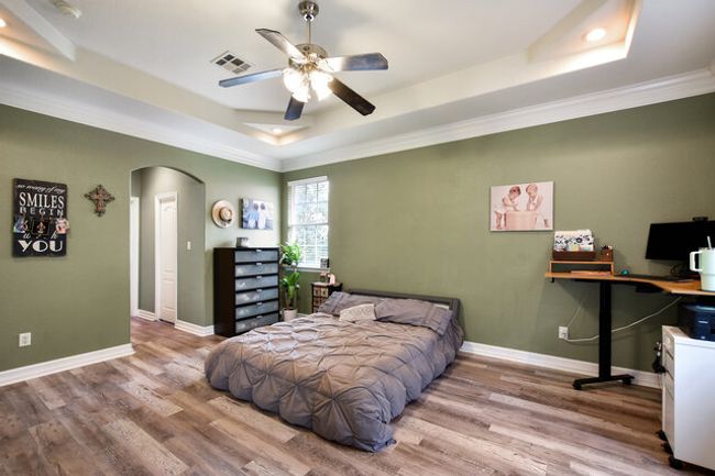 Bedroom featuring a raised ceiling, arched walkways, wood finished floors, crown molding, and a desk | Image 17
