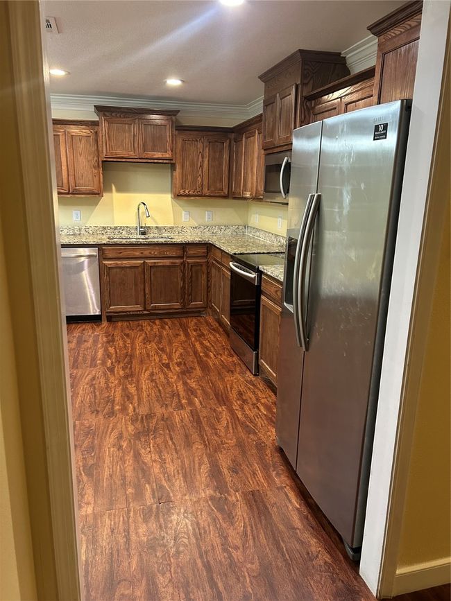 Kitchen featuring dark wood finished floors, refrigerator, ornamental molding, dishwashing machine, and stove | Image 7