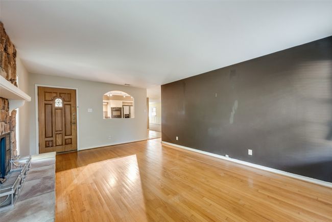 living room featuring a stone fireplace, baseboards, light wood finished floors, and arched walkways | Image 6