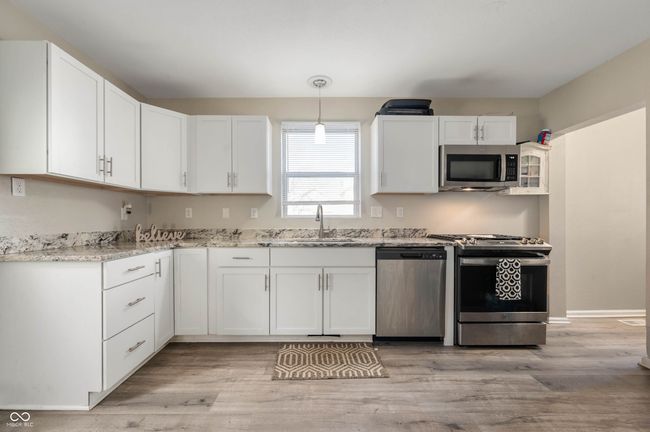 kitchen featuring a sink, light wood-type flooring, white cabinetry, stainless steel appliances, and light stone counters | Image 11