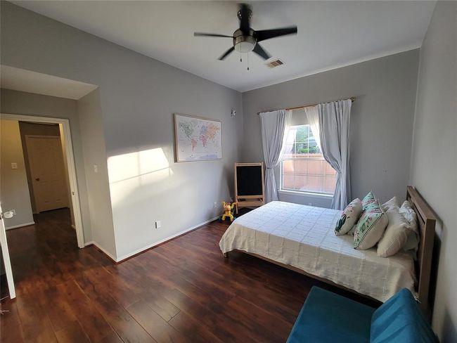 This spacious bedroom features hardwood floors, a large window with natural light, and neutral gray walls. | Image 23