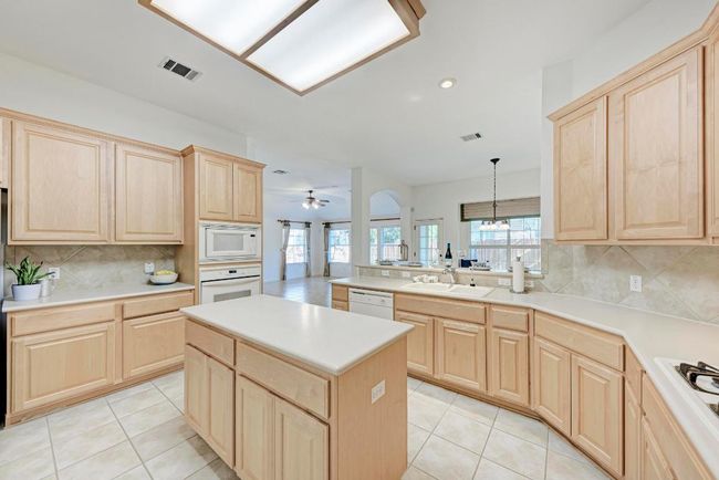 Kitchen with white appliances, light tile patterned floors, visible vents, a sink, and light brown cabinetry | Image 18