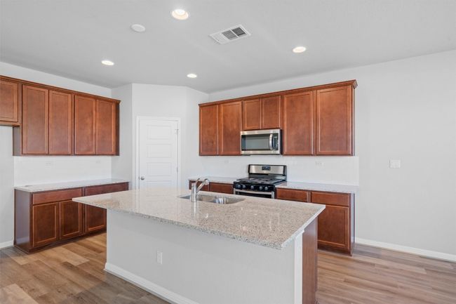 Kitchen with appliances with stainless steel finishes, light wood-style floors, recessed lighting, a kitchen island with sink, and light stone countertops | Image 9