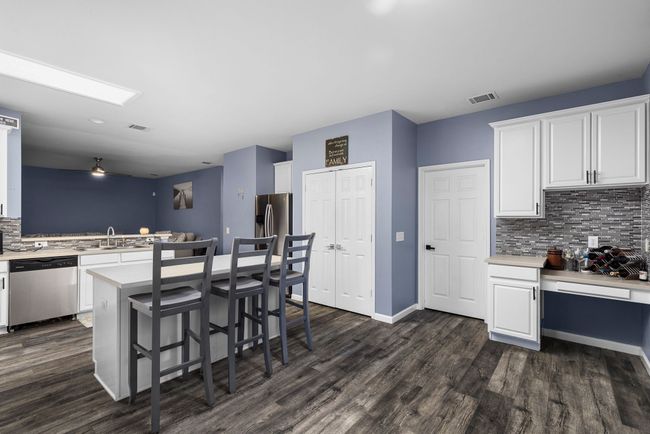 Kitchen with white cabinets, appliances with stainless steel finishes, a breakfast bar, and dark wood-type flooring | Image 16
