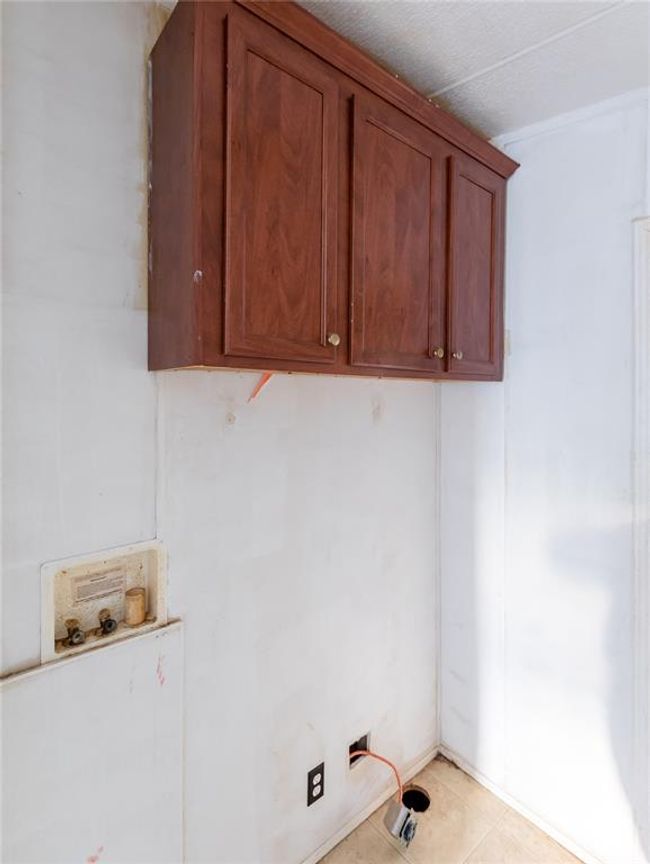 Clothes washing area with hookup for a washing machine, light tile patterned floors, and cabinets | Image 8