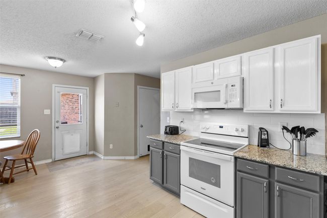 Kitchen with white appliances, gray cabinetry, decorative backsplash, a textured ceiling, and light wood-style floors | Image 9