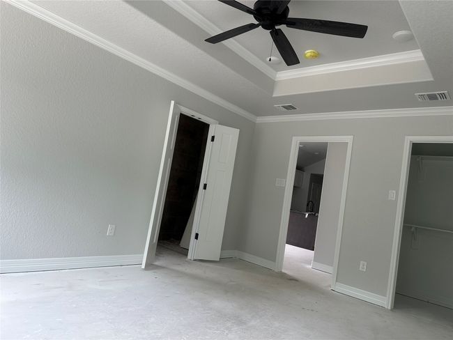 Unfurnished bedroom with a walk in closet, crown molding, visible vents, concrete flooring, and a raised ceiling | Image 8