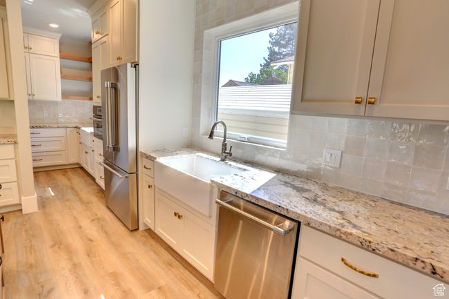 Kitchen with appliances with stainless steel finishes, backsplash, light wood-style floors, light stone counters, and white cabinetry | Image 12