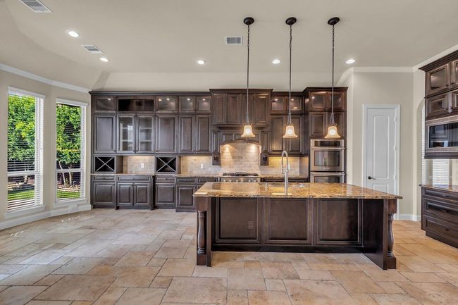 The top cabinets showcase elegant glass doors with interior lighting, beautifully illuminating displayed dishware and décor. This stylish feature adds depth and sophistication to the kitchen. | Image 10