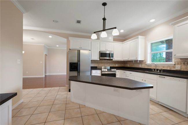 Kitchen with stainless steel appliances, a sink, decorative backsplash, arched walkways, and white cabinetry | Image 7