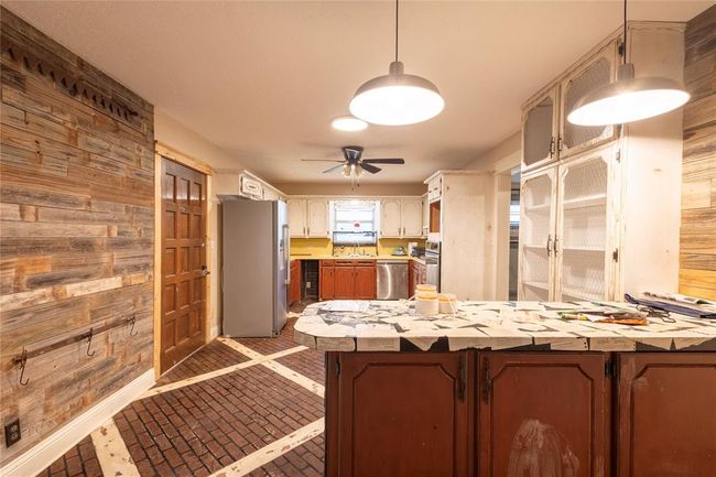 Kitchen with stainless steel appliances, wooden walls, brick patterned flooring, light countertops, and ceiling fan | Image 6