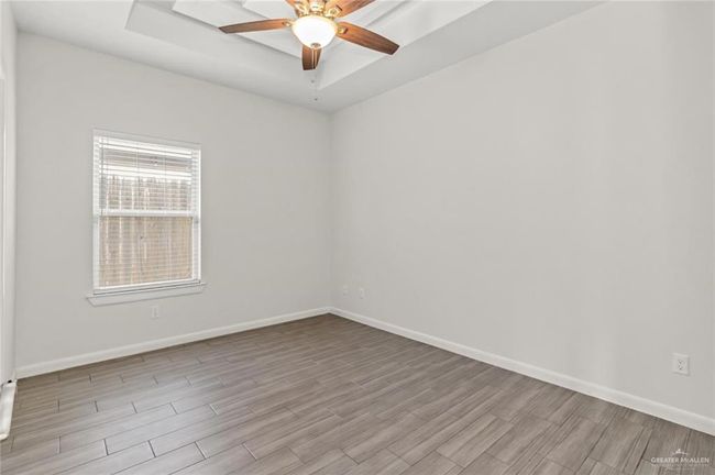 Empty room featuring wood finished floors, ceiling fan, and a raised ceiling | Image 7