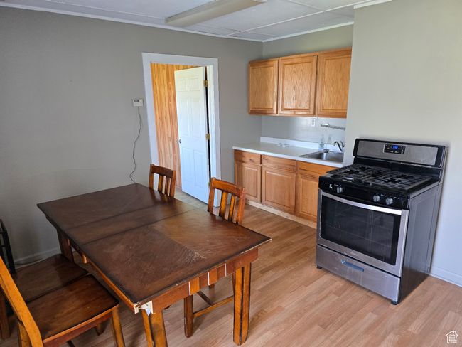 Kitchen with light wood-type flooring, light countertops, a sink, and gas range | Image 9
