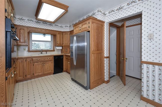 Kitchen with a sink, wallpapered walls, stainless steel fridge, light floors, and black dishwasher | Image 27
