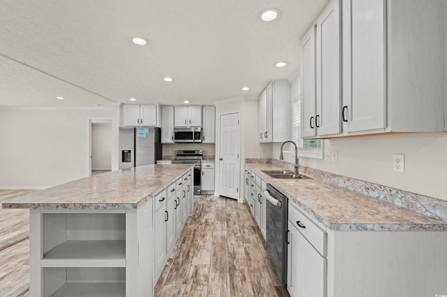 Kitchen with light countertops, a center island, appliances with stainless steel finishes, and a sink | Image 12